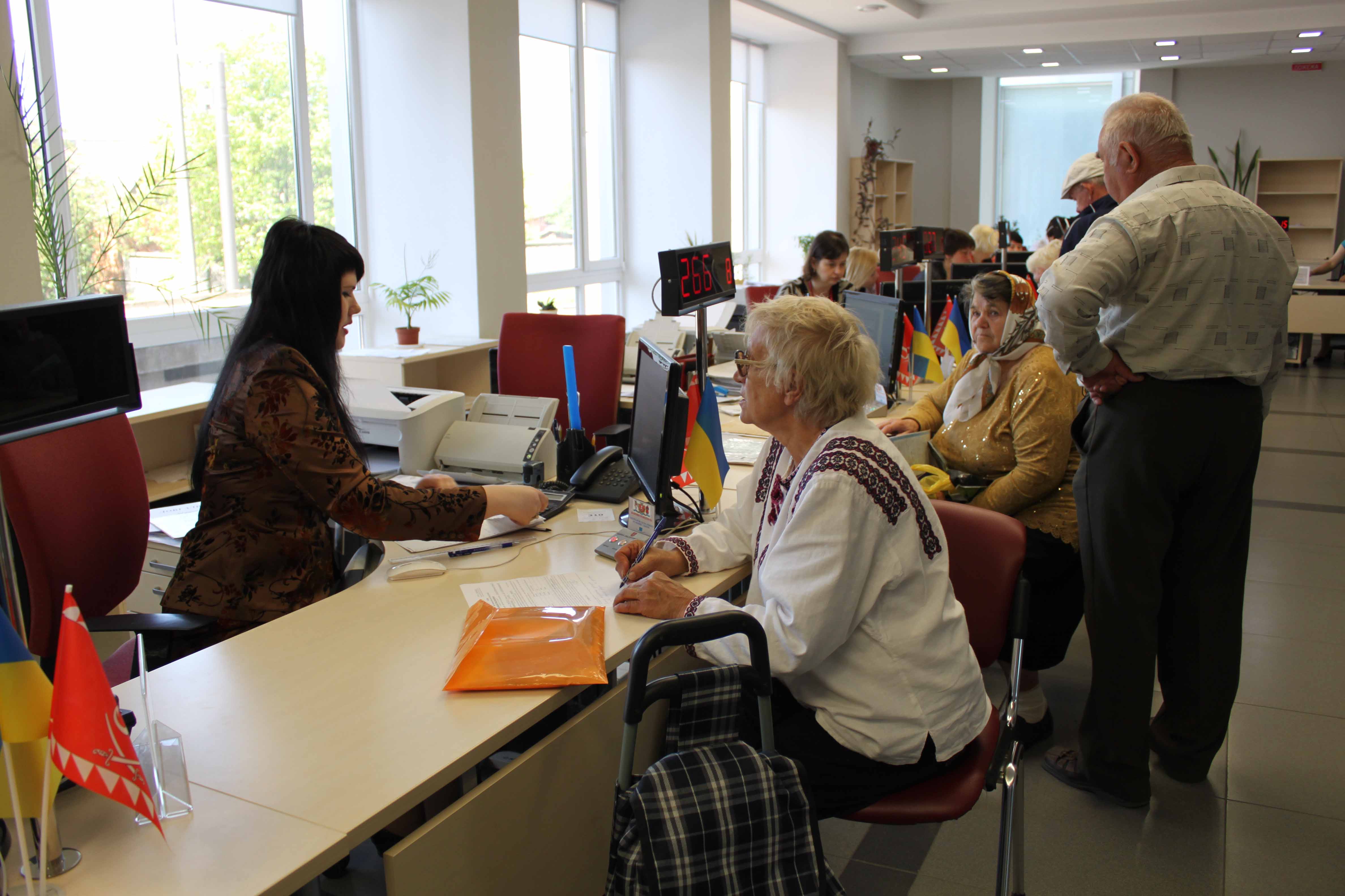 Su una fila di postazioni di lavoro, impiegati parlano con varie persone. 