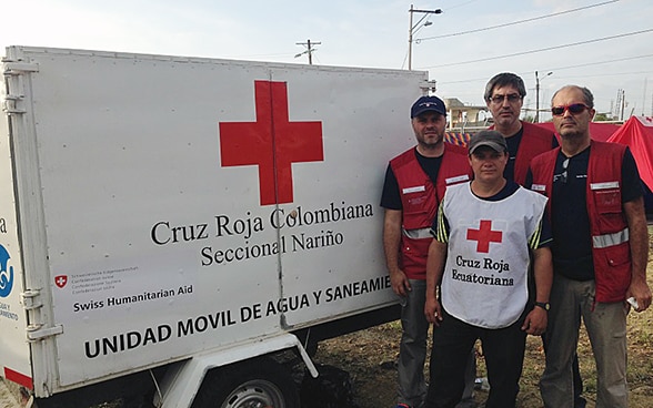 Trois membres du Corps suisse d’aide humanitaire et un collaborateur de la Croix-Rouge équatorienne posent devant une remorque transportant de l’eau potable. 