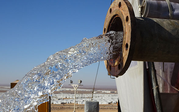 De l’eau coule d’une conduite avec le camp de réfugiés d’Azraq en arrière-plan. 