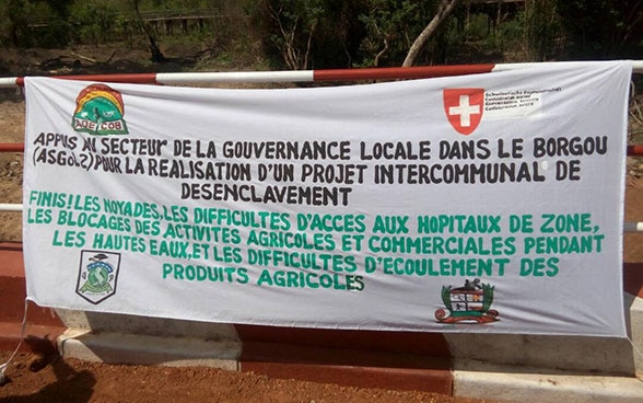 Photo d’une banderole indiquant «Finis! Les noyades, les difficultés d’accès aux hôpitaux et les blocages des activités agricoles et commerciales pendant les hautes eaux.»