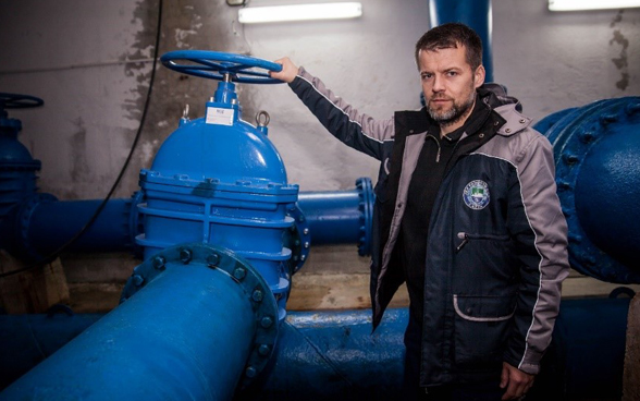 A man standing in front of a blue gate valve connected to a large blue pipe.