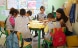 Inside a classroom where a woman teacher is sitting in front of a group of children showing them a book.