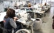 In a large room, five women sit one behind the other at sewing machines and sew.