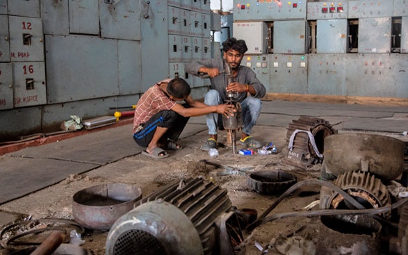The picture shows two men from Nepal who are squatting and screwing on a machine.