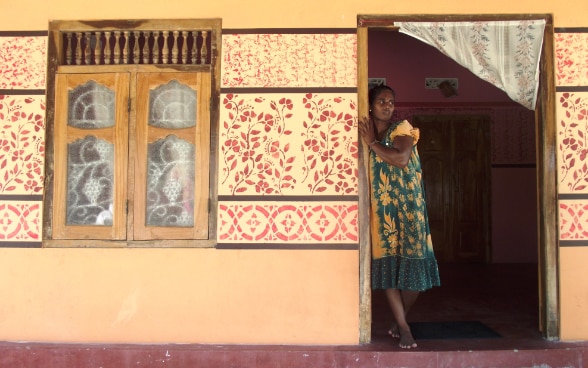Une femme sri-lankaise se tient dans l’embrasure de la porte d’entrée de sa maison.