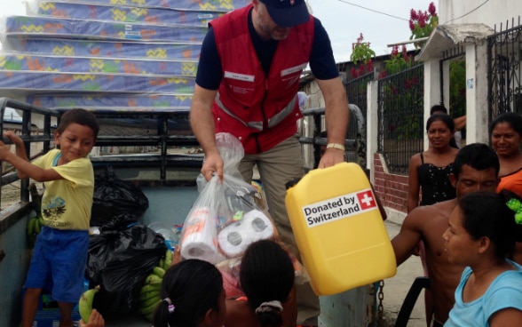 A Swiss expert handing a jerrycan of drinking water to children from the back of a truck.