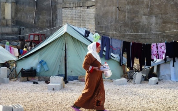 A woman refugee walks in front of a tent.