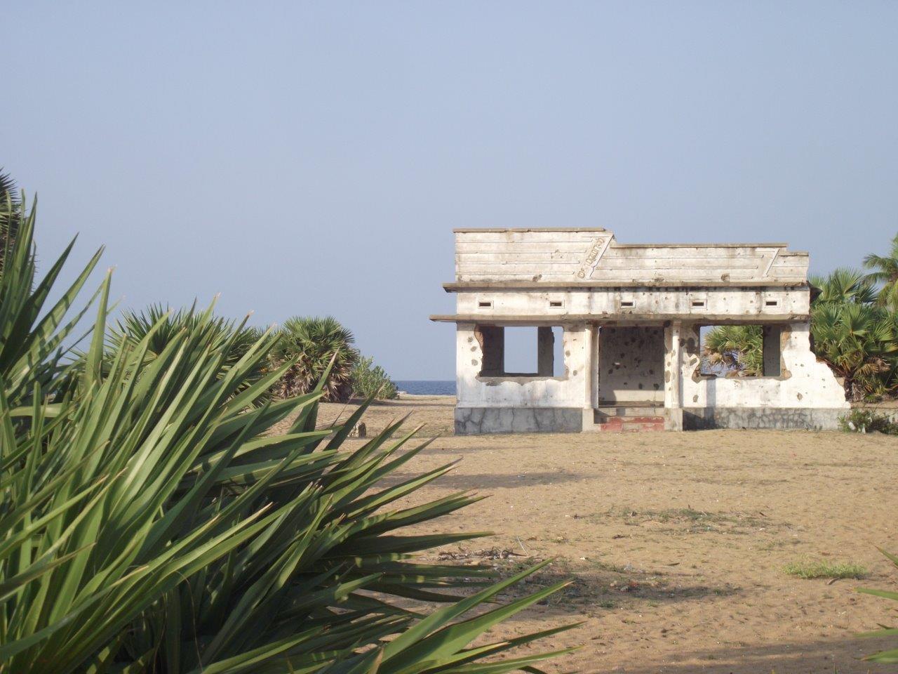 Vista de una casa situada al borde del océano, destruida y llena de impactos de bala.