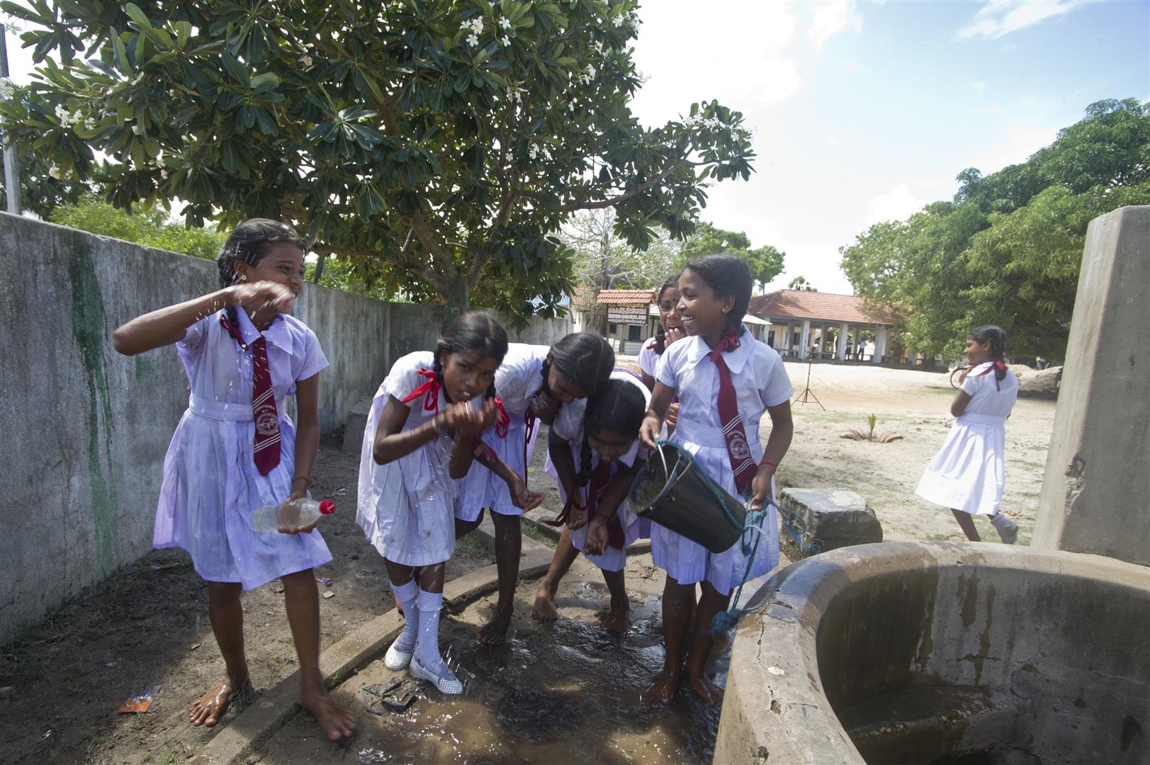 Un grupo de escolares bebiendo agua al borde de un pozo.