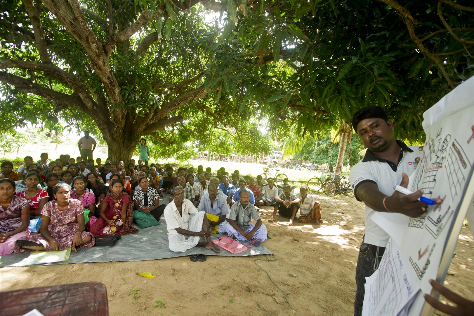 Un colaborador de la COSUDE expone un proyecto de construcción a varias decenas de aldeanos sentados en esteras.