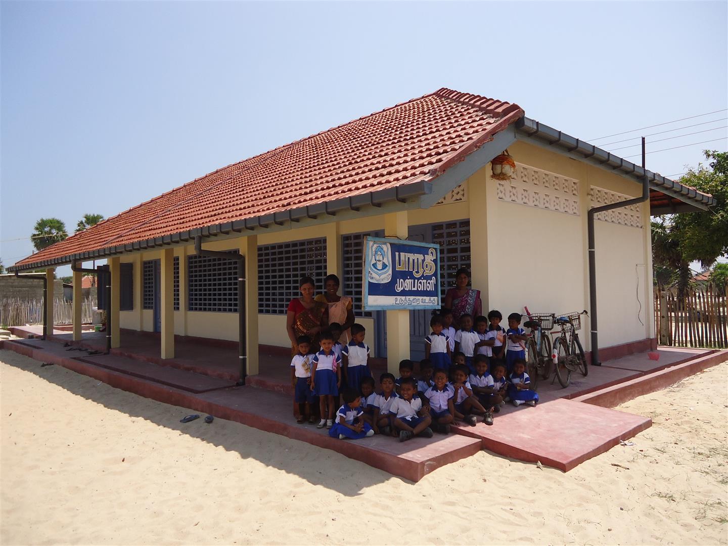 Un grupo de párvulos posa con sus maestras delante de su flamante escuela.