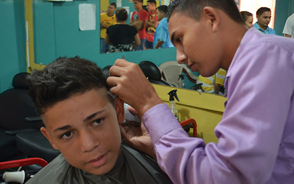 Un aprendiz de peluquero cortándole el cabello a un muchacho
