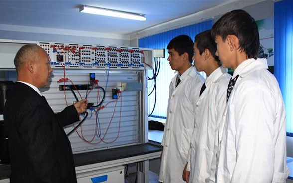 Un docente y tres aprendices frente a un tablero eléctrico