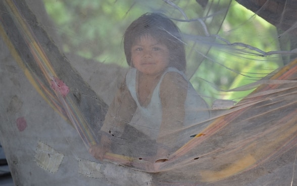 A child sitting in a hammock covered by a mosquito net.