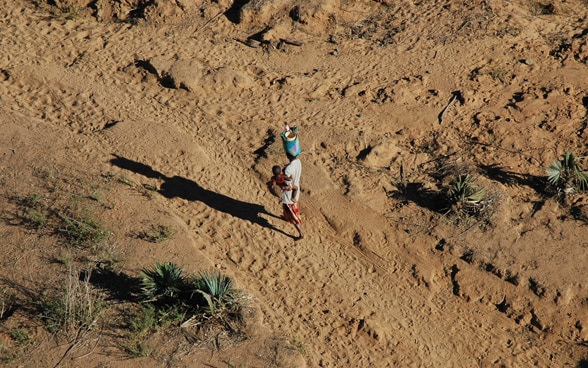 Woman walks in desert with child in her arms.