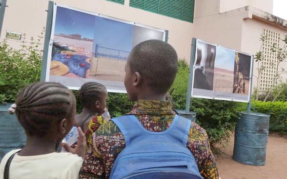 Trois enfants regardent une exposition de photos en extérieur.