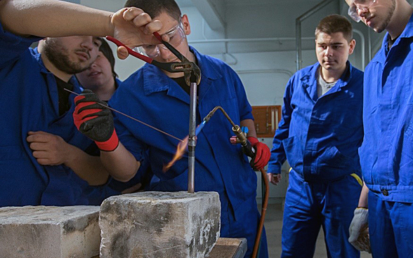  Des jeunes gens en bleu de travail observent un instructeur en train d’effectuer une soudure.