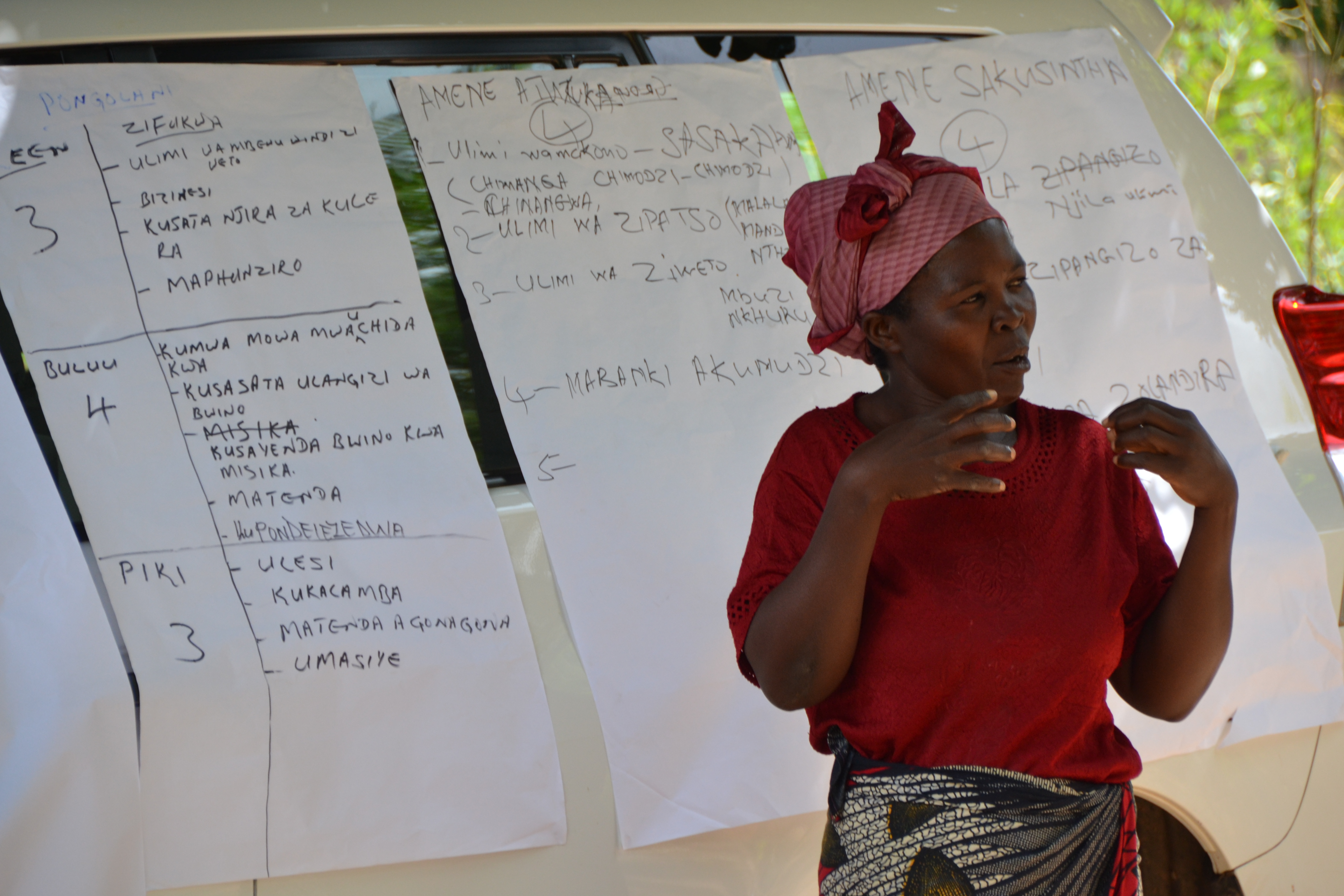 A woman standing in front of a car providing explanations. 