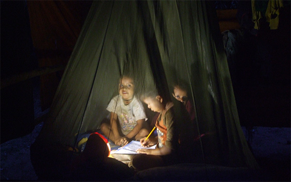 Trois enfants assis sur le sol font leurs devoirs.