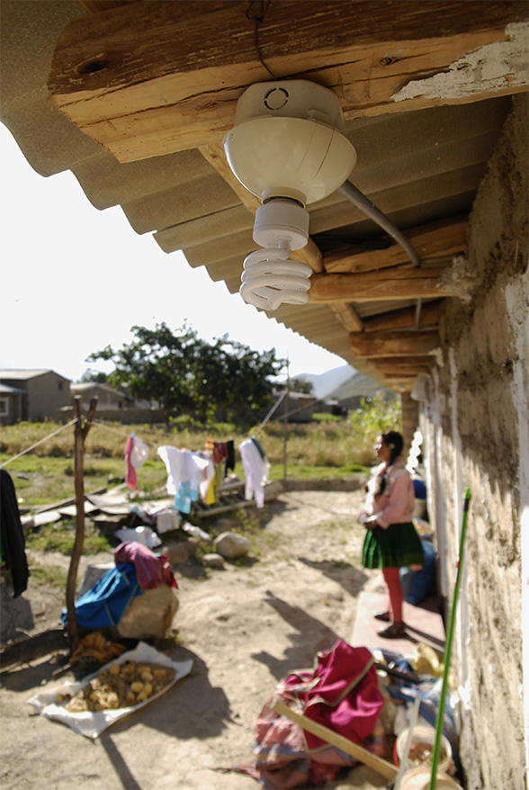 Eine Sparlampe hängt vom Dach eines Hauses. Im Hintergrund steht ein Mädchen.