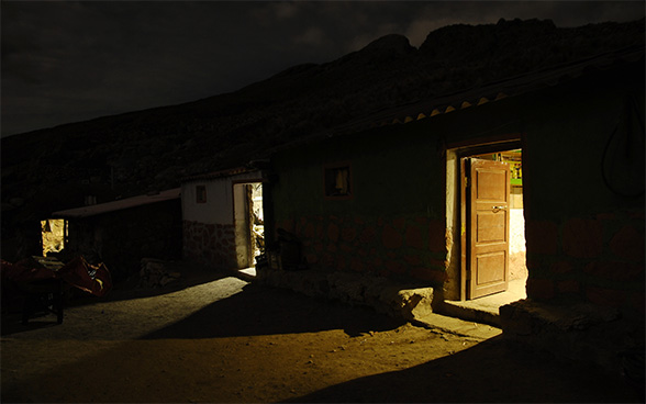 Une maison avec trois portes ouvertes dans le noir. Une lumière brille à l'intérieur.