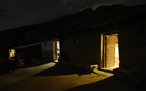 Ein Haus mit drei geöffneten Türen im Dunklen. Im Innern des Hauses brennt Licht.