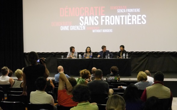 Quatre personnes sont assises sur une estrade dans une salle de cinéma. Des spectateurs se trouvent devant elles et les écoutent. 