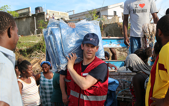 un expert suisse, entouré d’Haïtiens, distribue des bâches.