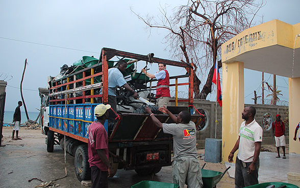 Des hommes déchargent un camion rempli de brouettes et d’outillages.