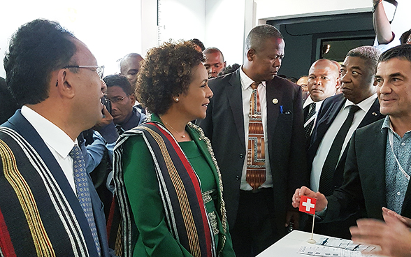 Der madagassische Präsident und die Generalsekretärin der Frankophonie besuchen den Schweizer Stand. Hinter ihnen stehen zahlreiche Journalisten.