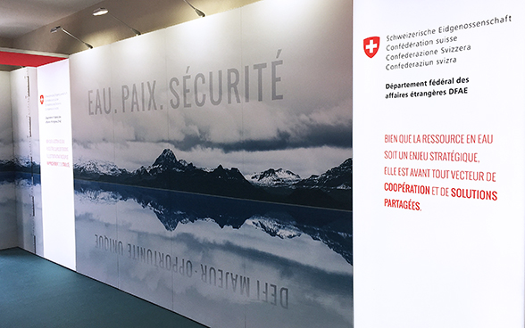 Eine grosse Plakatwand zeigt eine Berglandschaft. Auf dem Bild steht in grossen Lettern eau, paix und sécurité.
