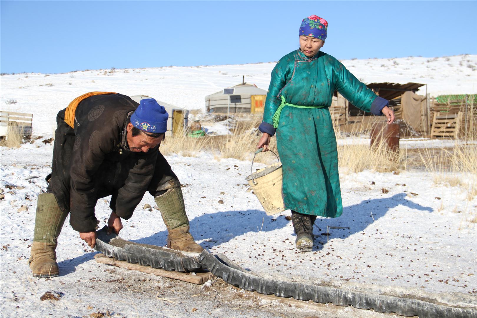 Homme construisant un abreuvoir et femme portant un seau d’eau pour le remplir.