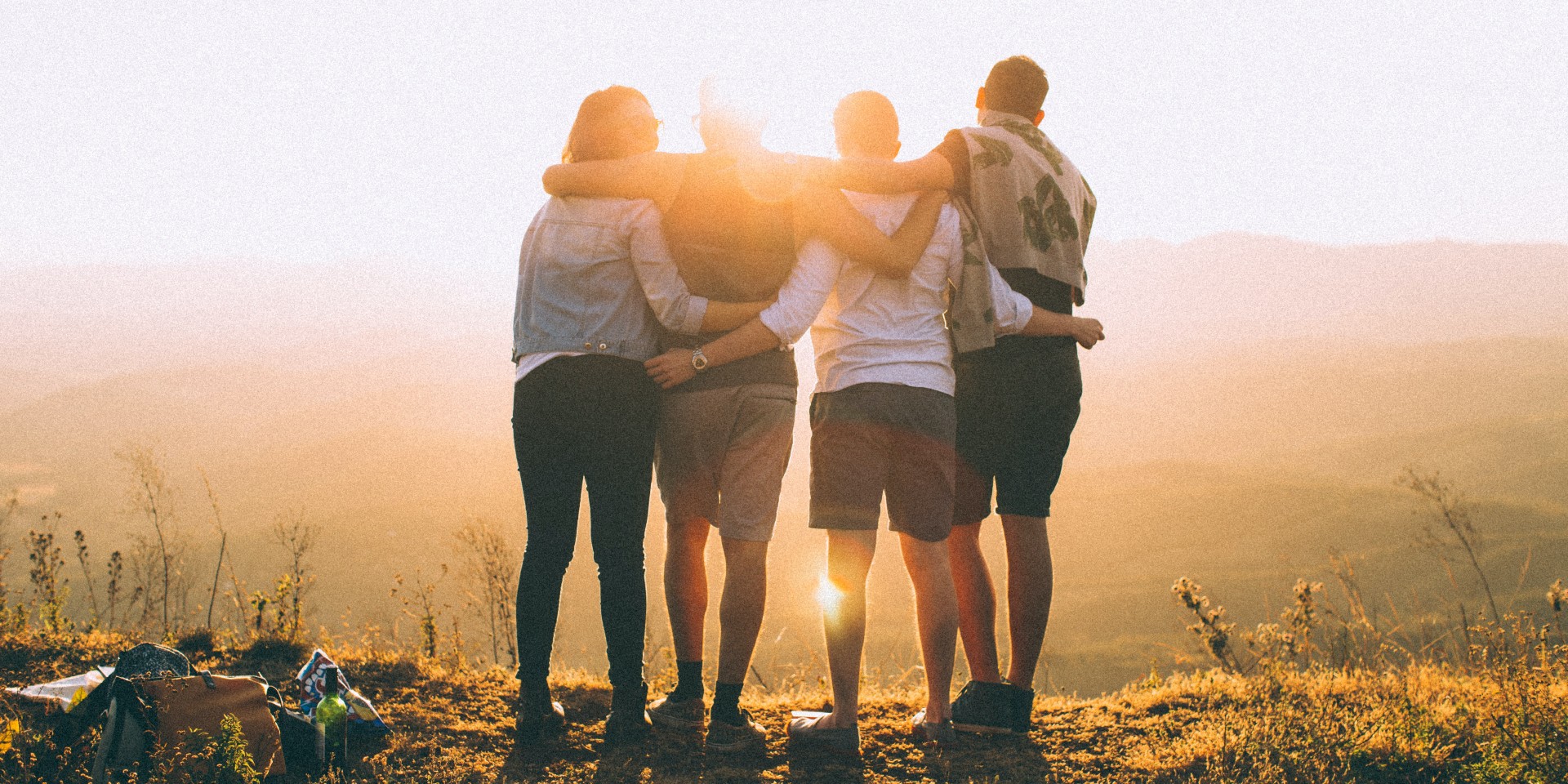 Four young people with their arms around each other watching the sunset from a viewpoint.