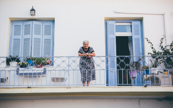 Eine alte Frau steht auf ihrem Balkon.