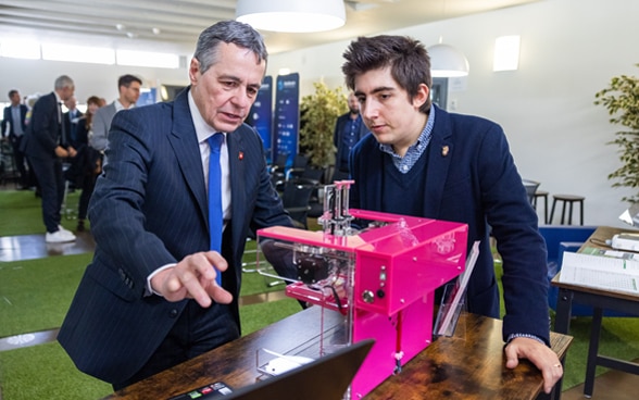 Un giovane mostra a Ignazio Cassis come funziona un macchinario. 