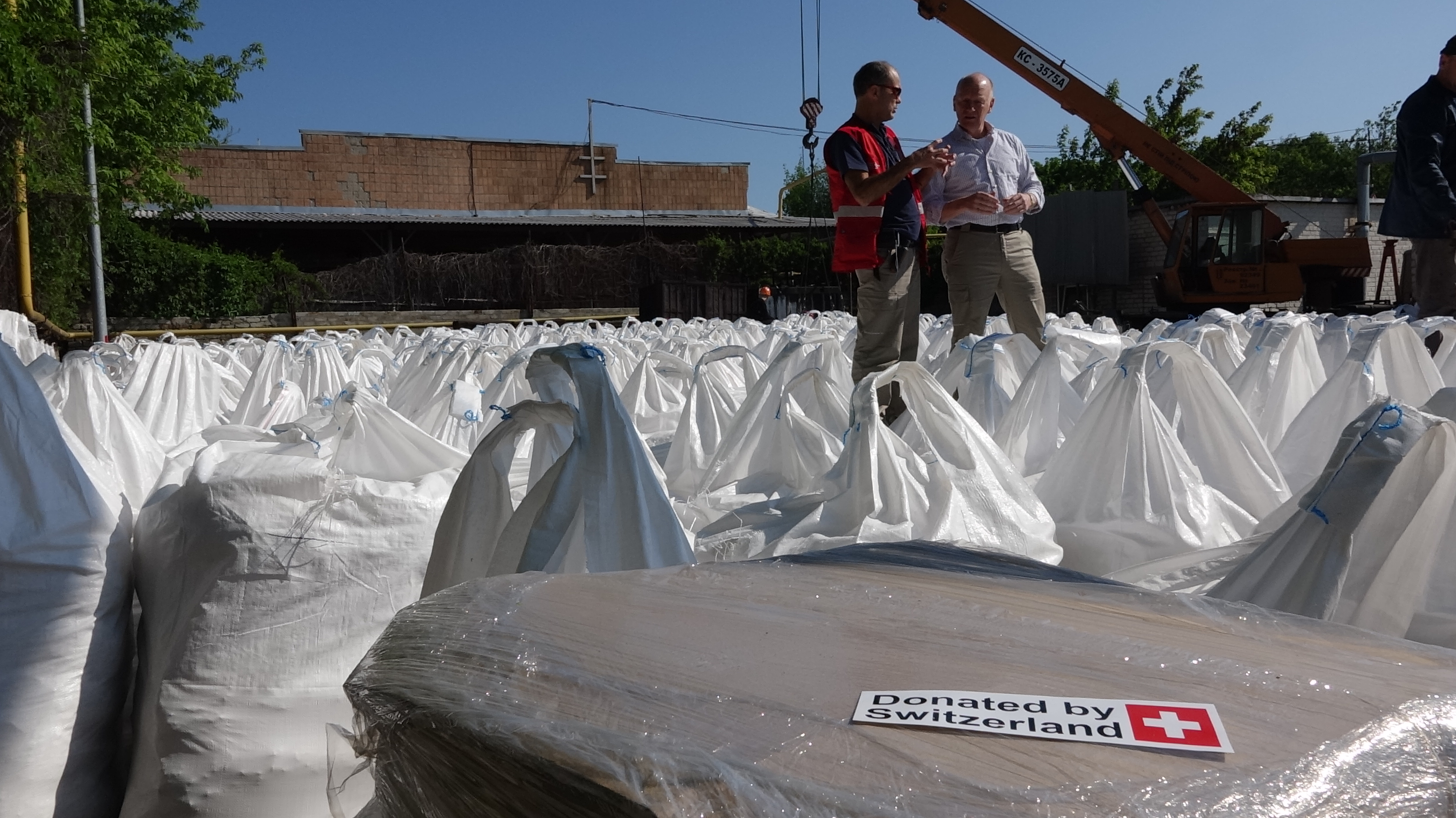 Zwei Schweizer Experten stehen inmitten Hunderter von Säcken mit Chemikalien, die auf dem Gelände eines Wasserwerks lagern.