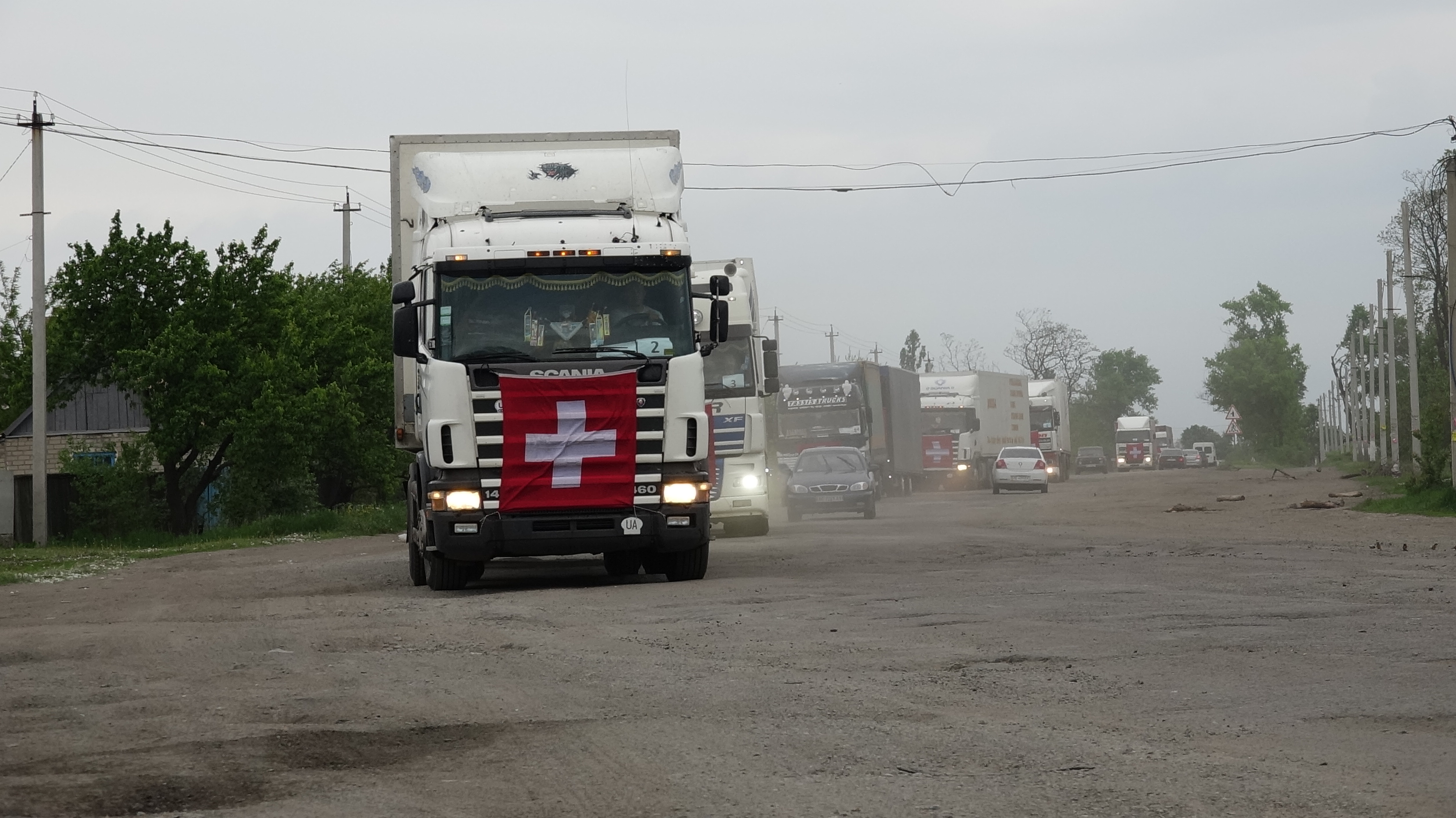 Alcuni camion con esposta la bandiera svizzera transitano su una strada.  