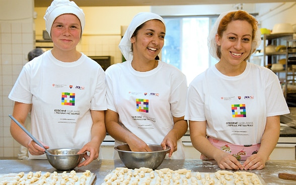 Drei junge Frauen in Ausbildung bereiten zwei Backbleche voller Gebäck zu. 