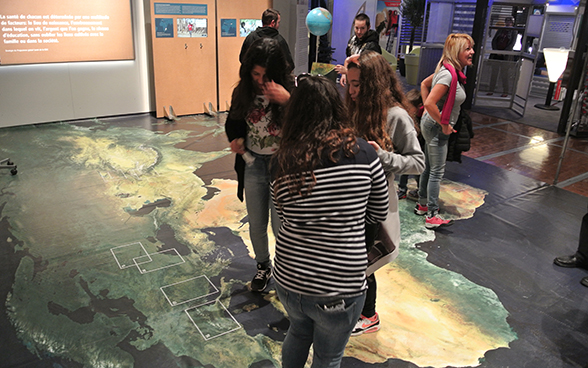 Un groupe d’adolescentes se déplace sur la carte du monde proposée sur le stand. © DFAE