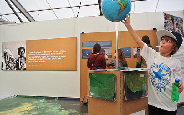 En primer plano, un niño observa un mapa del mundo instalado en el stand de la COSUDE. © DFAE