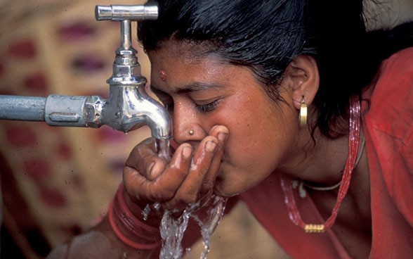 Une femme boit de l‘eau d’un robinet.