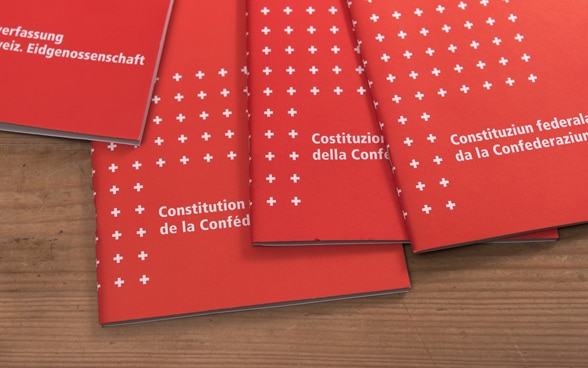 Posés sur un support en bois, quatre exemplaires de la Constitution fédérale suisse dans chacune des langues nationales.
