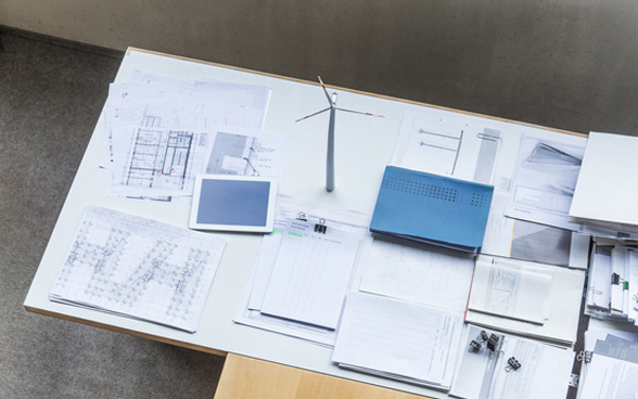 Modèle réduit d’éolienne, plans de construction et tablette sur un bureau.