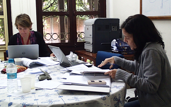 Deux collaboratrices de l'Ambassade de Suisse au Népal travaillent autour d'une table où se trouvent des ordinateurs et des documents. 