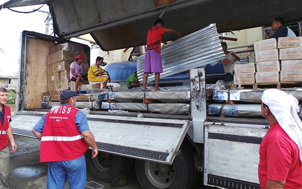 Angehörige des Schweizerischen Korps für Humanitäre Hilfe entladen zusammen mit Bewohnern der Insel Leyte auf den Philippinen einen Lastwagen mit Gütern der Humanitären Hilfe