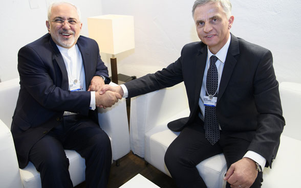 Bundesrat Didier Burkhalter und der iranische Aussenminister Mohammad Javad Zarif sitzen auf am WEF 2017 auf weissen Sesseln und geben sich die Hand.