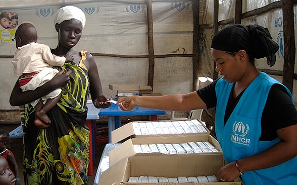 A woman with a child is given a voucher for food in a United Nations tent.