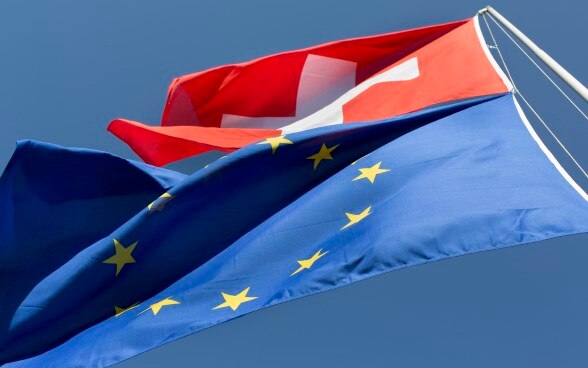 The flags of Switzerland and the European Union flying from one flag pole.