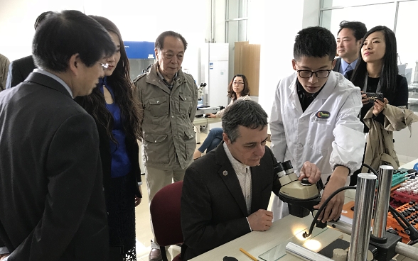 Bundesrat Ignazio Cassis sitzt vor einem Mikroskop. Er ist umgeben von Studierenden der chinesischen Akademie der Wissenschaften.