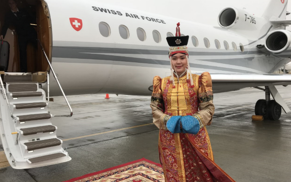 A woman in traditional dress poses in front of the Swiss Air Force plane at Ulaanbaatar airport